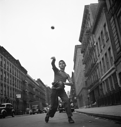 Young boy tossing a ball on a city street.